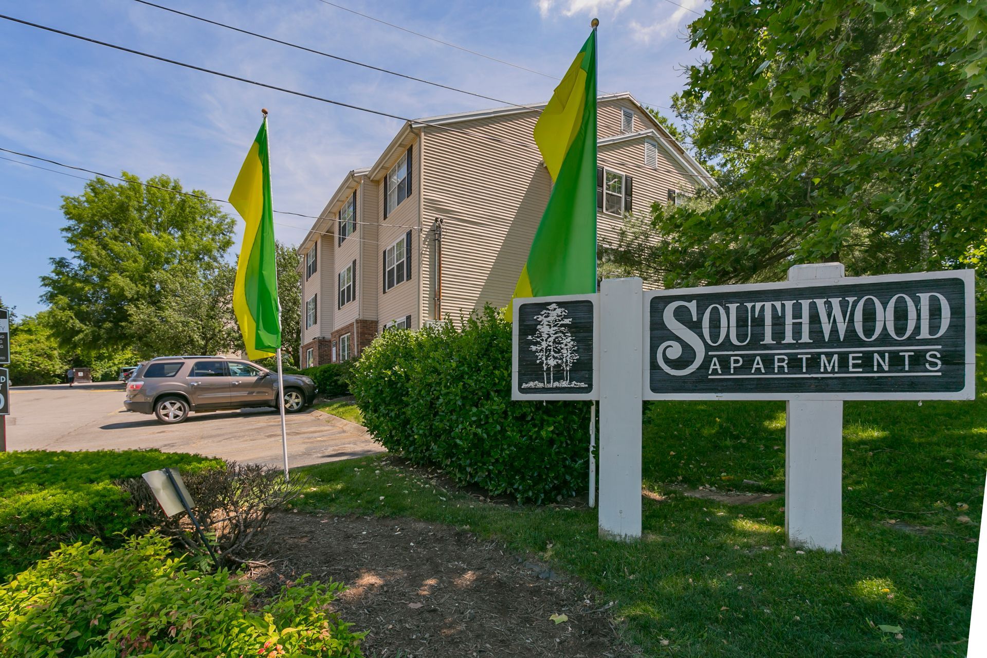 A sign for Southwood Apartments sits on a grassy lawn in front of a multi-story building and a parked SUV.