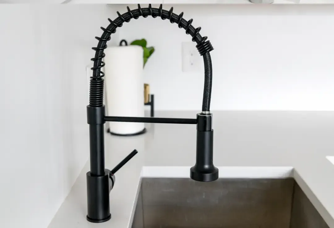 Black kitchen faucet over a stainless steel sink installed by 17 plumbing,  with a paper towel holder in the background.