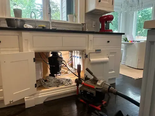Kitchen drain clog cleared by emergency plumber Oakville using professional equipment Emergency plumber Oakville clearing clogged kitchen drain with professional equipment under sink
