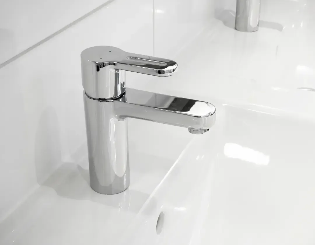 Shiny chrome faucet in a white bathroom sink. The faucet is turned off.