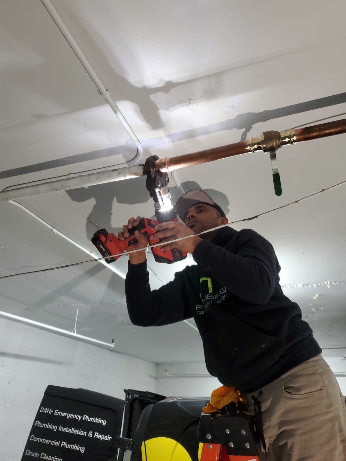 A man is working on a pipe with a drill in a garage.