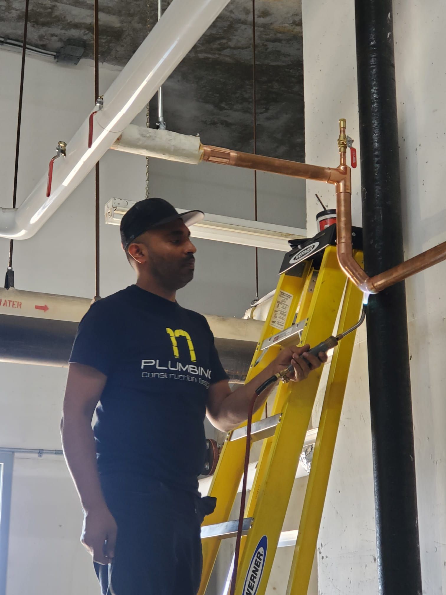 A man is standing on a ladder working on pipes.