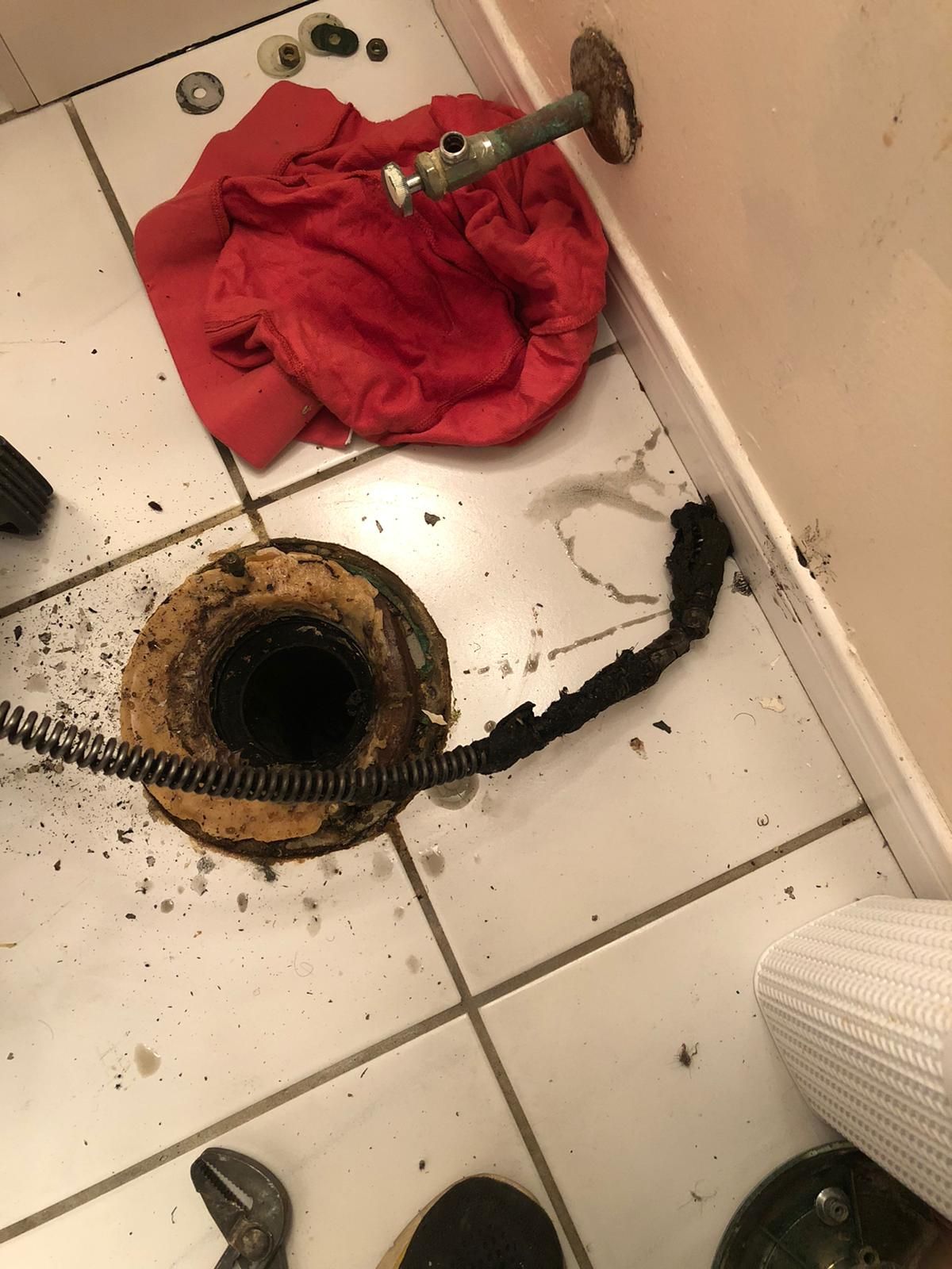 A toilet with a hose coming out of it and a red towel on the floor.