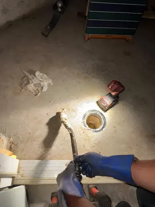 Hands in blue gloves lighting a torch near a floor drain in a dim indoor workspace