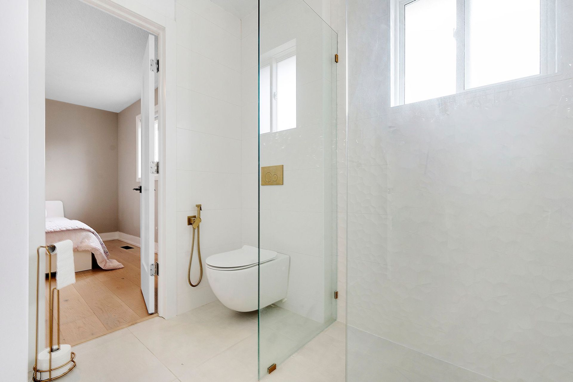 Minimalist white bathroom design featuring wall-hung toilet, glass shower enclosure, and matte gold bidet spray in Oakville home by 17 Plumbing Team