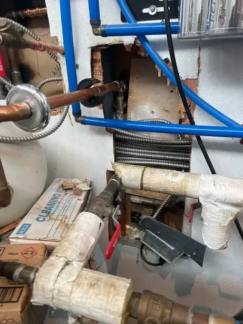 Electrical and plumbing access panel opened to assess domestic hot water leak behind the wall