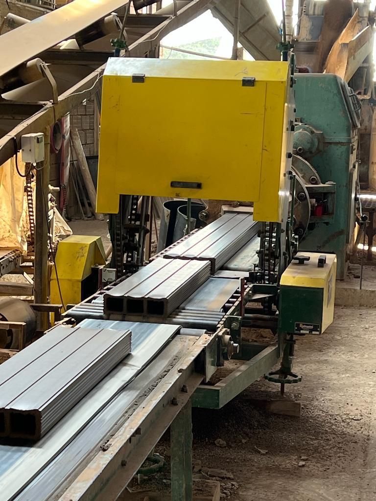 Sierra industrial amarilla cortando vigas de metal en un taller.