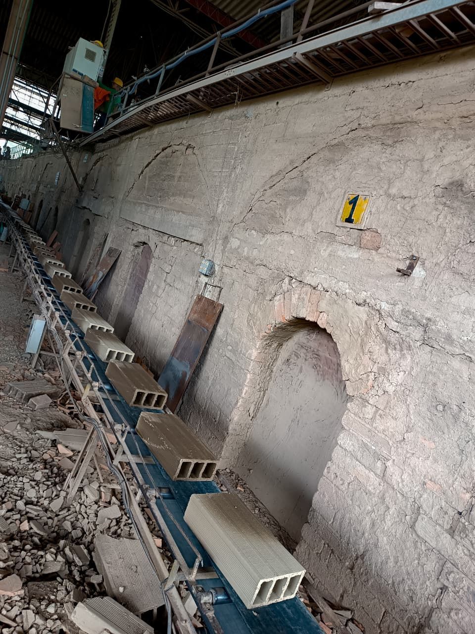 Muro de hormigón dañado en una obra en construcción con escombros, soportes y andamios elevados.