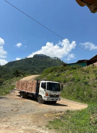Camión de carga blanco en un camino de tierra junto a una ladera verde bajo un cielo azul