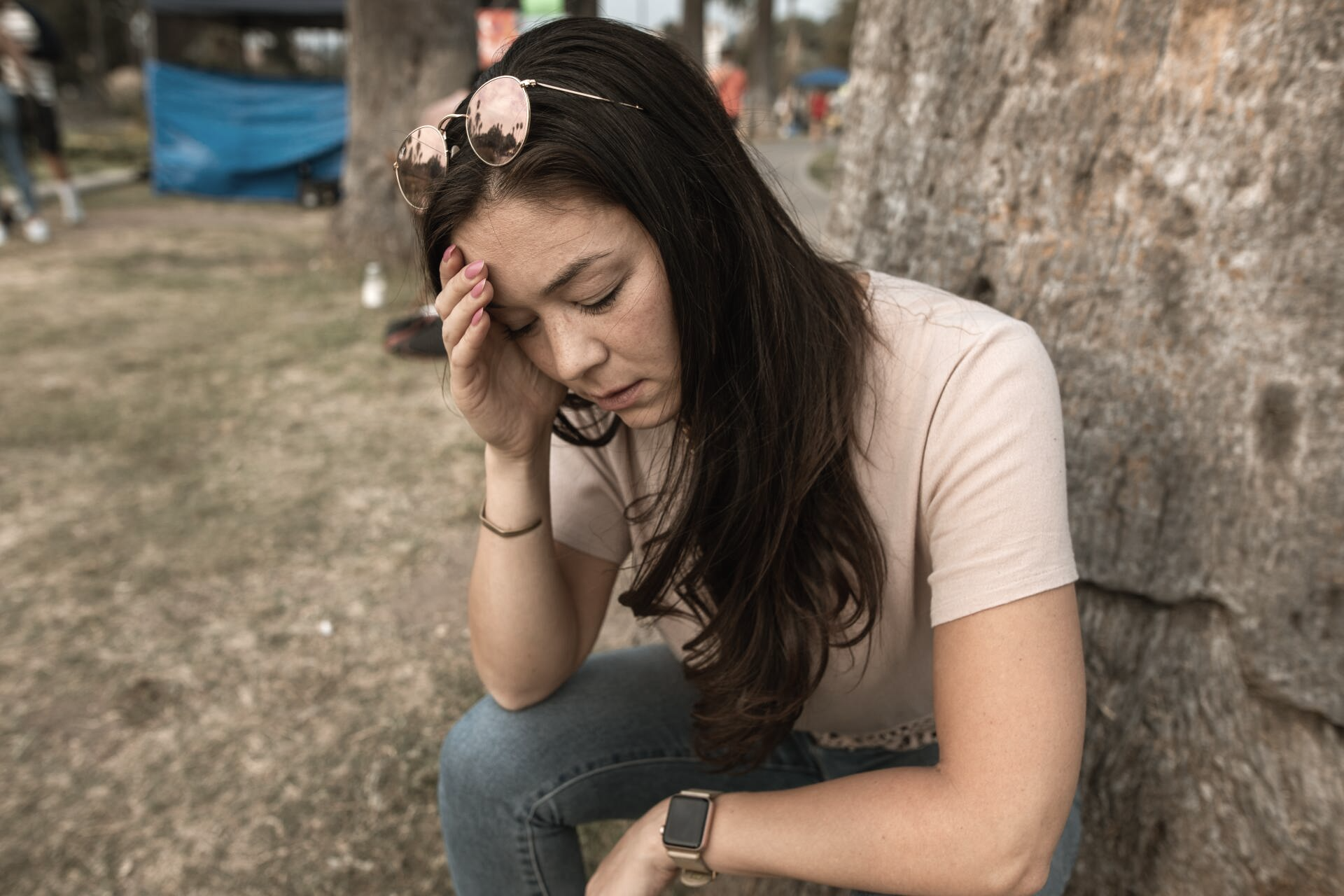 A woman is sitting on the ground with her head in her hands.