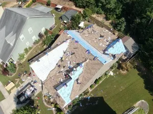 Aerial view of a roof under repair with blue tarps and scattered shingles around a house
