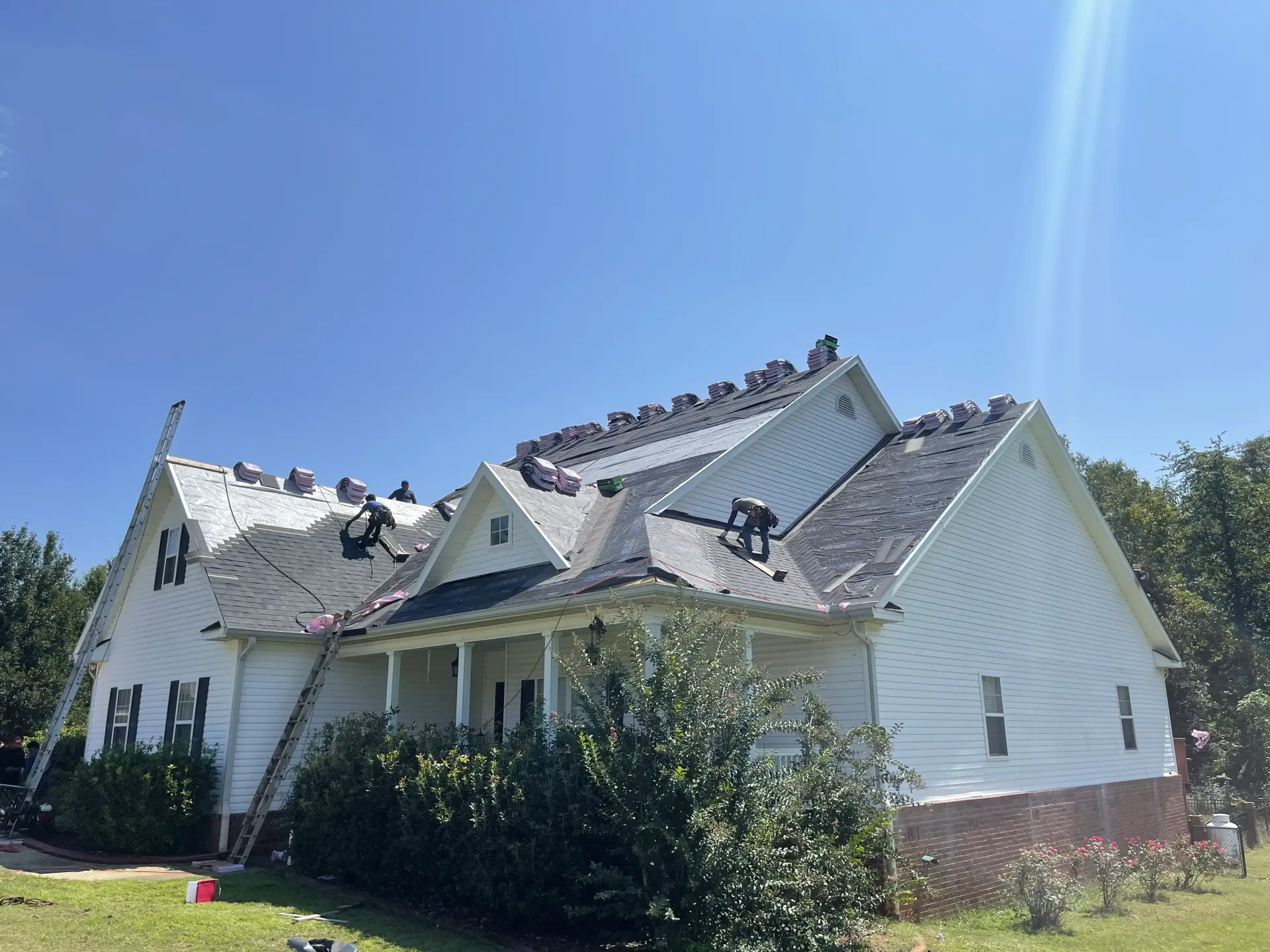 Damaged white house with collapsed roof and debris under a clear blue sky
