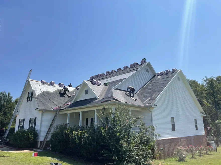Severely damaged white house with torn roof and debris, under a clear blue sky.