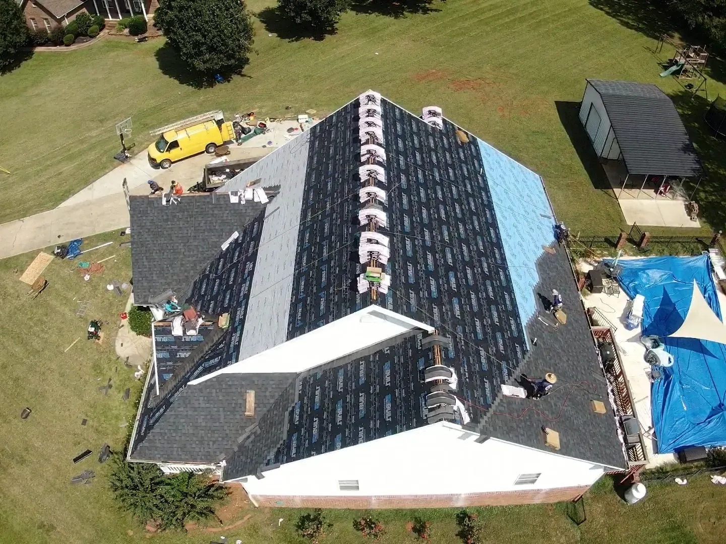 Aerial view of a house roof under construction with workers, tools, and a yellow truck nearby