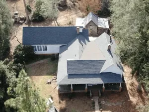 Aerial view of a house with a dark roof, light walls, and surrounding trees and yard
