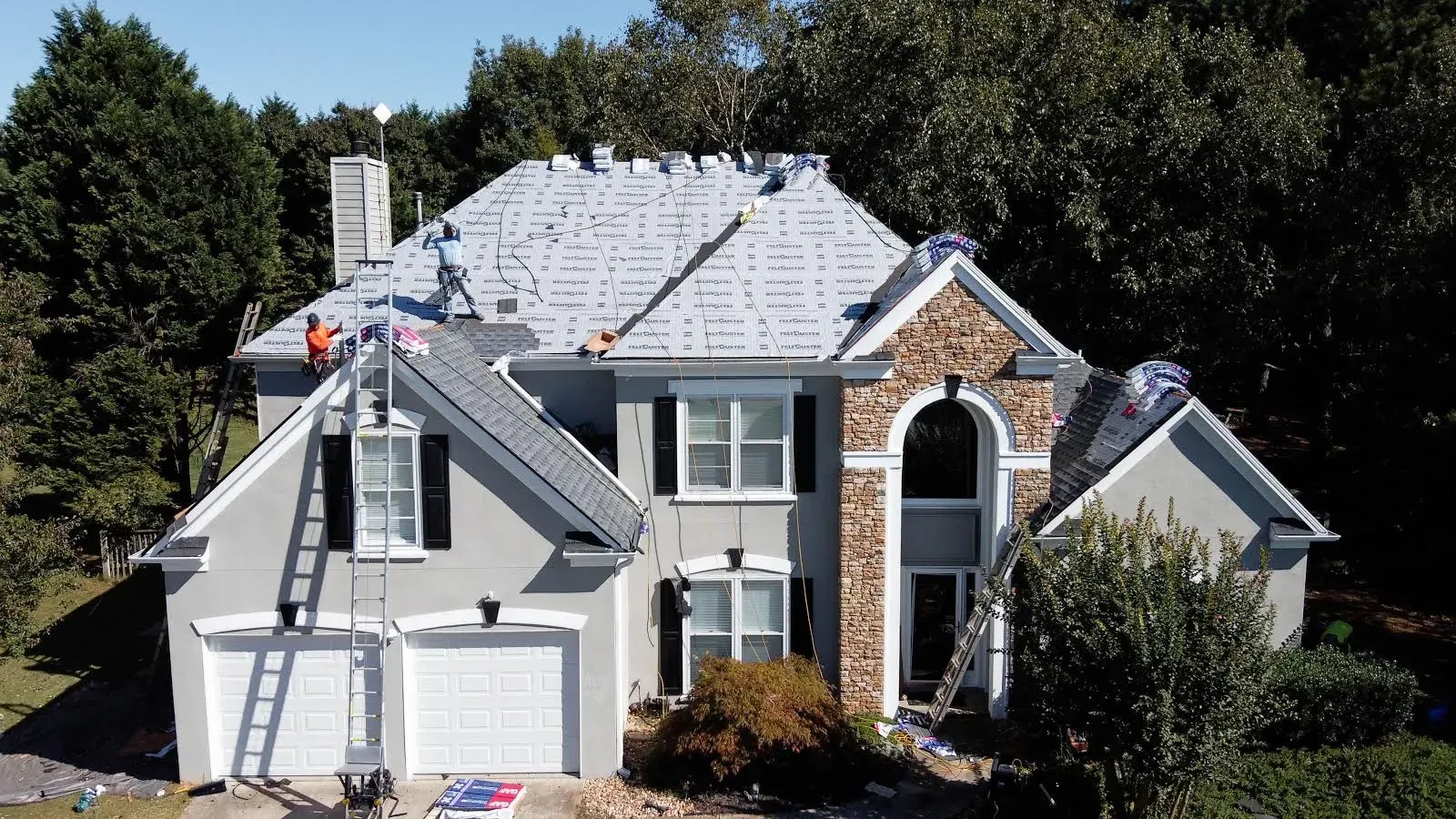 Workers roofing a white two-story suburban house with ladders and an attached garage