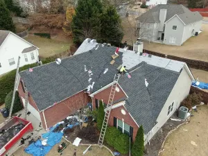 Aerial view of a house roof under repair with workers and scattered roofing materials.