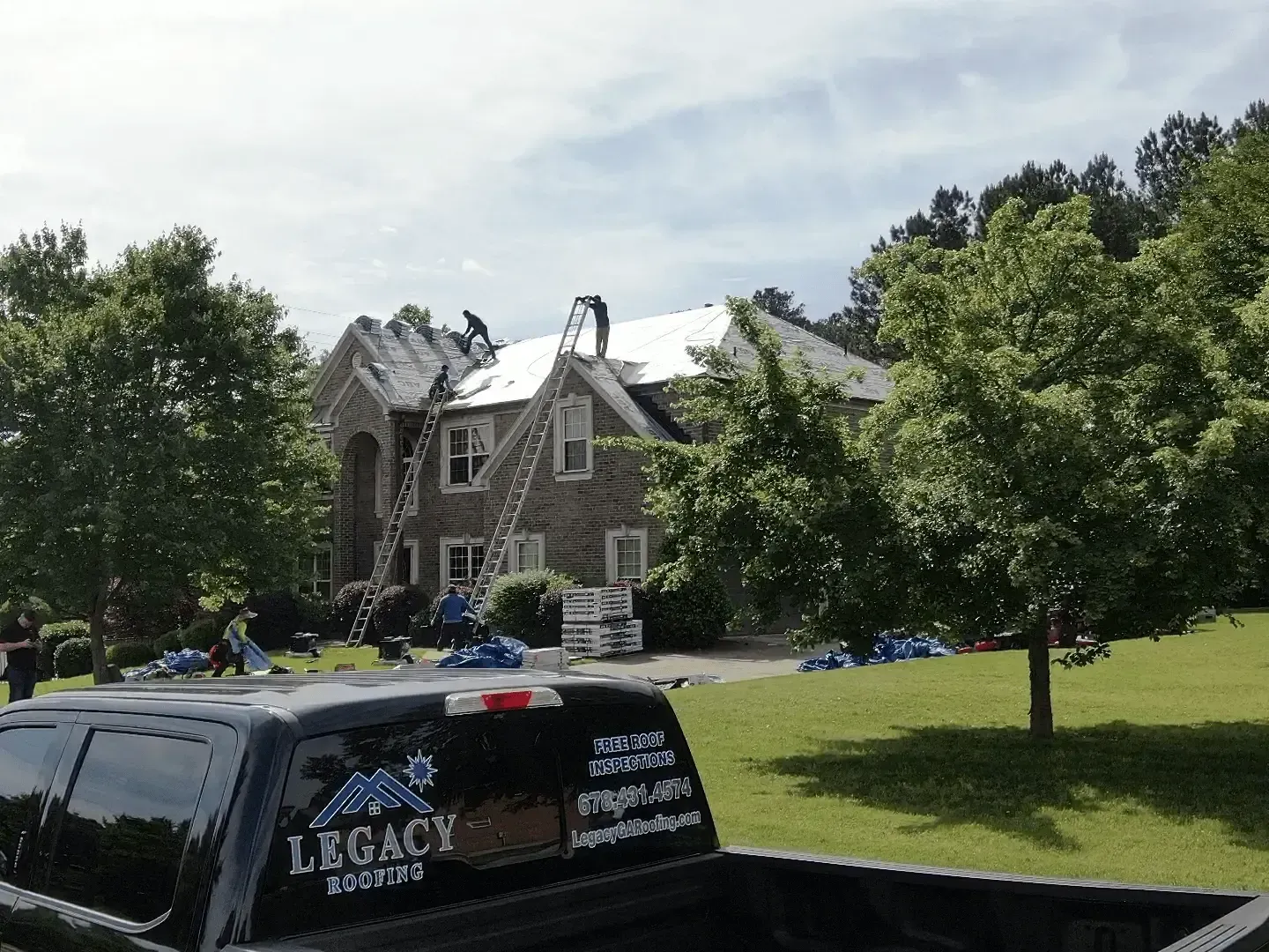 Stone mansion behind trees with a black van parked on a green lawn under a bright sky