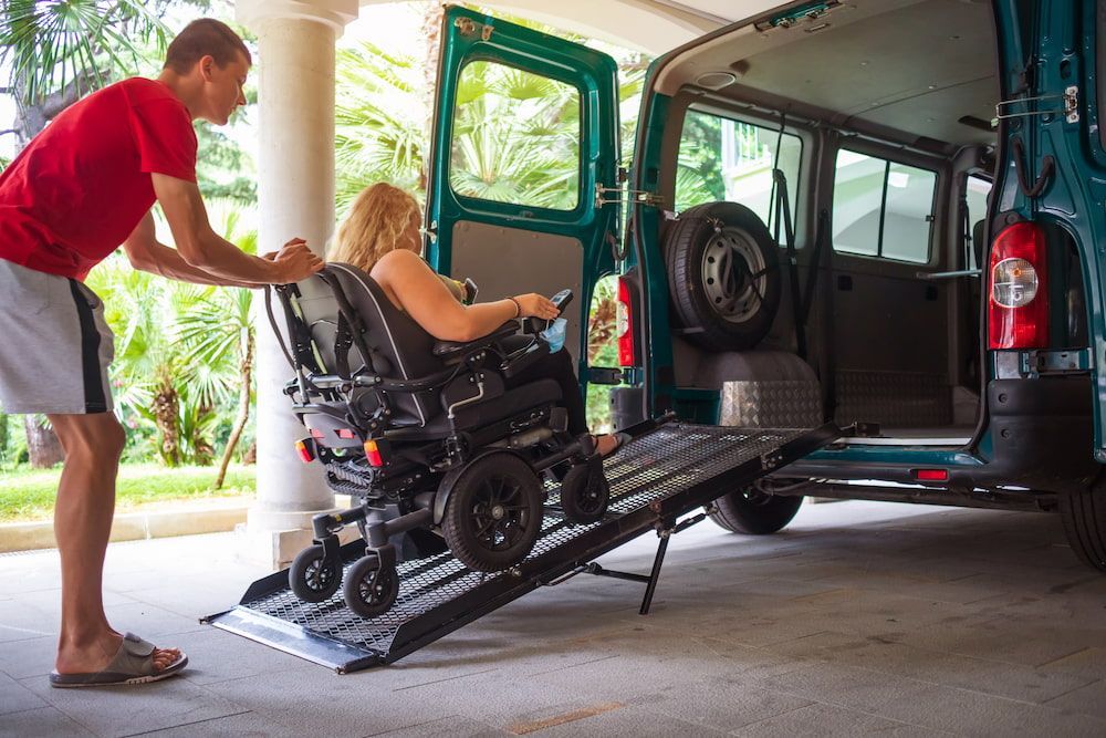 A Man is Helping a Woman in a Wheelchair Get Into a Van — Care FNQ Pty Ltd in Atherton, QLD