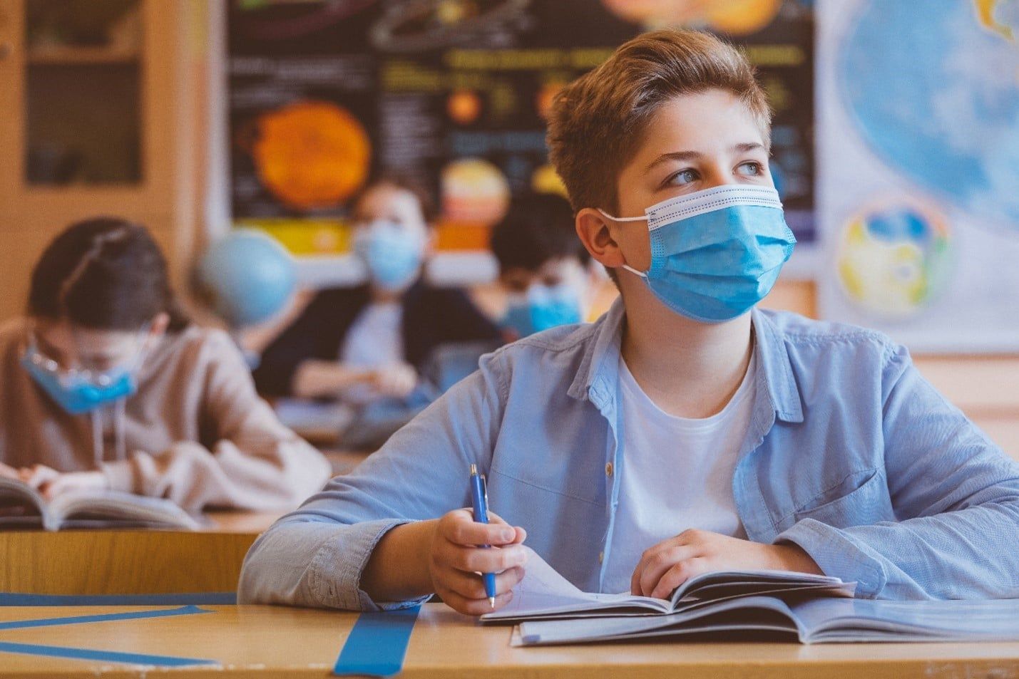 Boy Wearing a Face Mask is Sitting at a Desk in a Classroom — Care FNQ Pty Ltd in Atherton, QLD