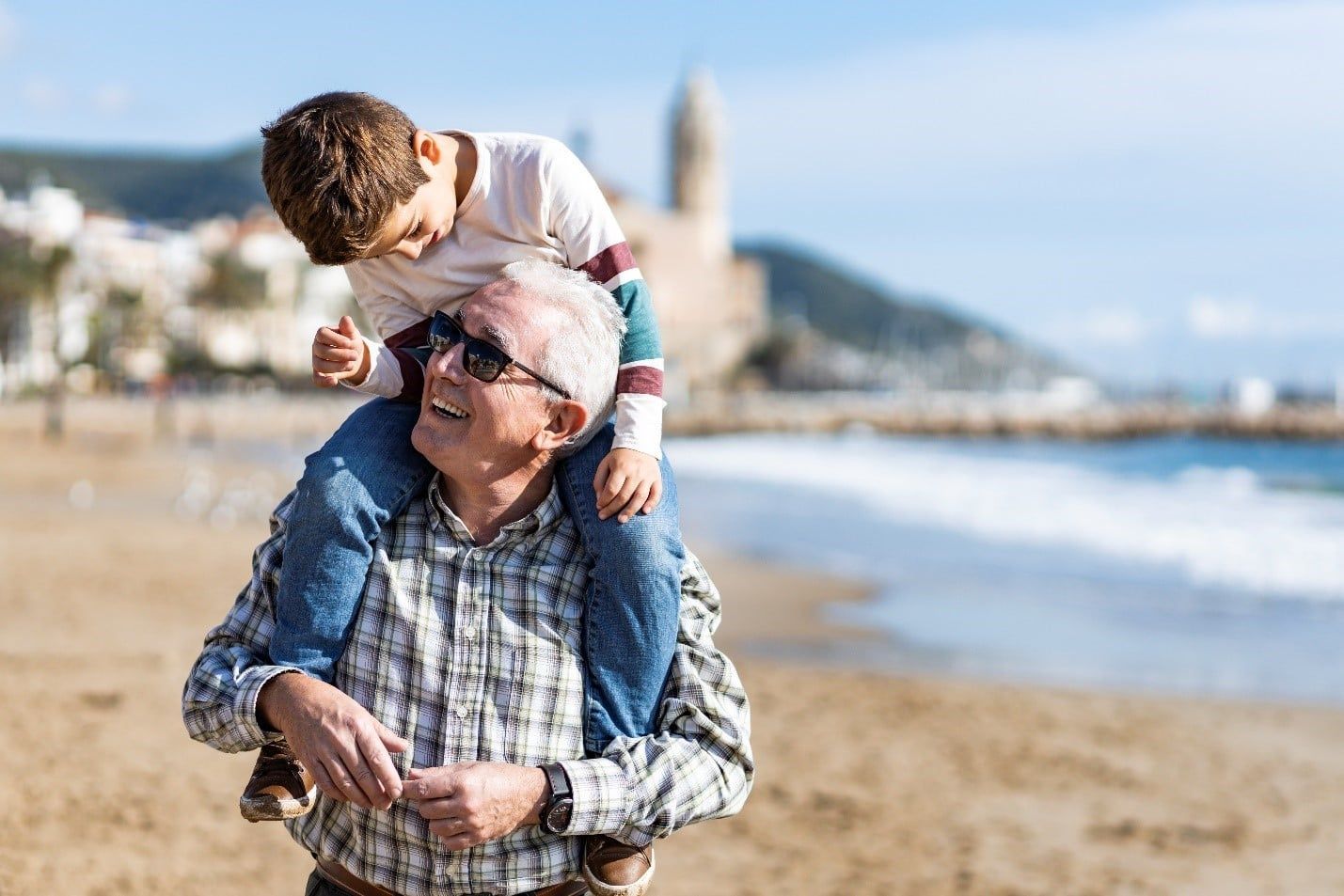 Elderly Man is Carrying a Young Boy on His Shoulders on the Beach — Care FNQ Pty Ltd in Atherton, QLD