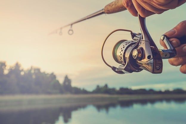 Person is Holding a Fishing Rod in Front of a Lake — Care FNQ Pty Ltd in Cairns City, QLD