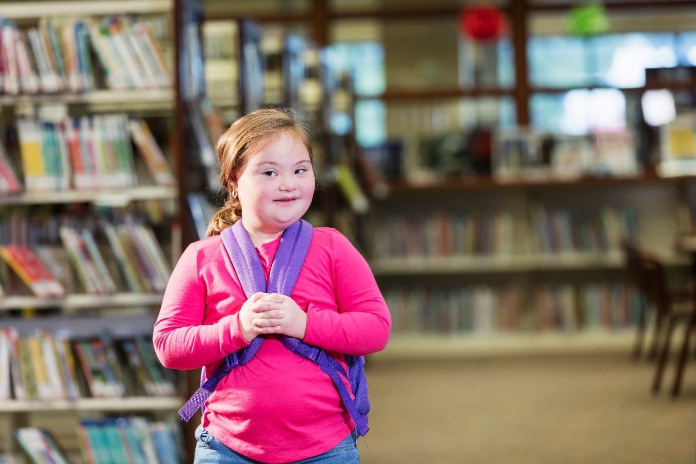 Little Girl is Standing in a Library Wearing a Backpack — Care FNQ Pty Ltd in Cairns City, QLD