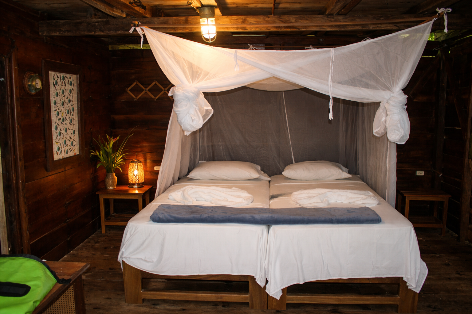 Dormitorio con dos camas, mosquitera, paredes de madera, mesitas de noche y linterna.