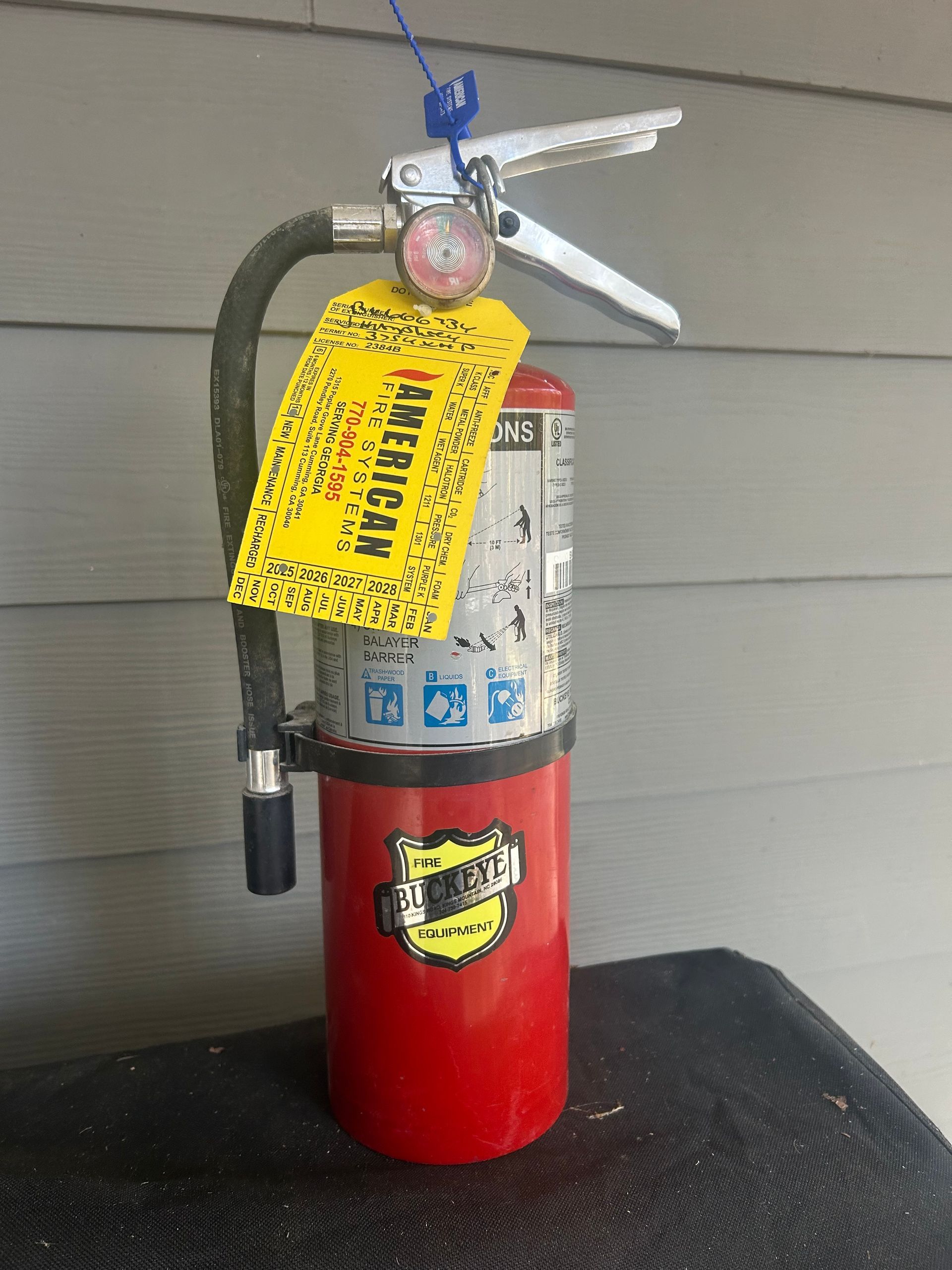 Red fire extinguisher with a yellow inspection tag, standing against a gray wall.
