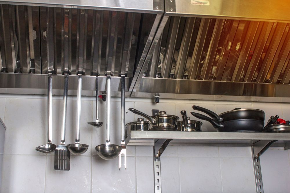 Stainless steel kitchen with hanging utensils and pots on shelves under a vent hood