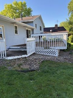 White house backyard with a small wooden deck and ramp, gravel path, and green lawn under a clear blue sky