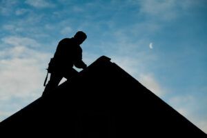 Silhouette of a person working on a rooftop against a partly cloudy sky with a crescent moon.