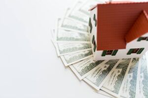 Toy house on a fan of hundred dollar bills, white background.