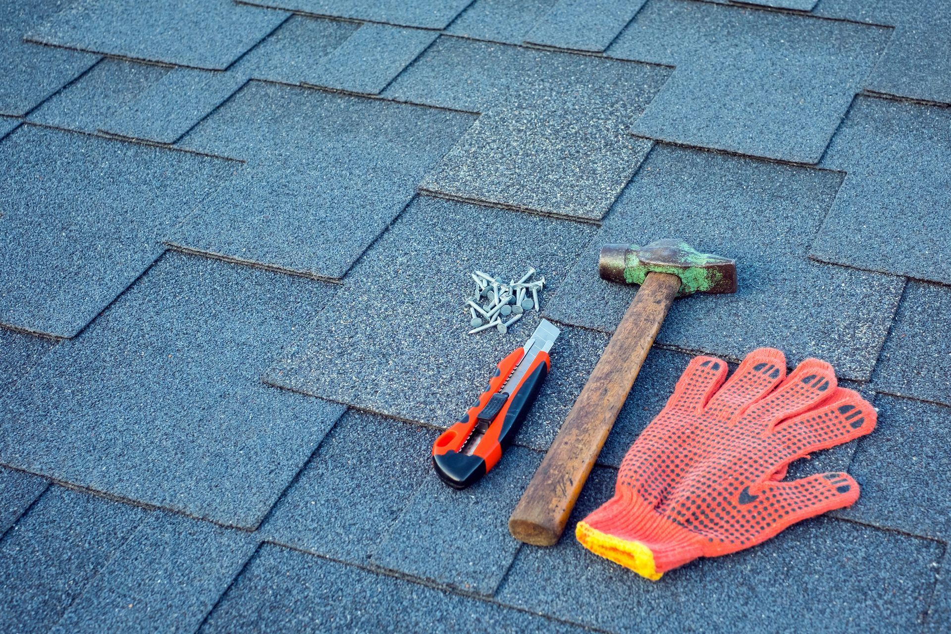 Close-up showcasing roofing contractor tools with asphalt shingles, hammer, nails, and utility knife.