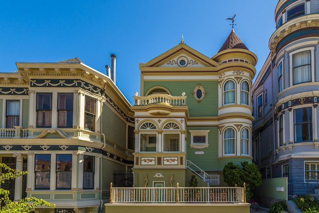 Colorful Victorian houses in San Francisco, green and cream facade with a turret under a blue sky.
