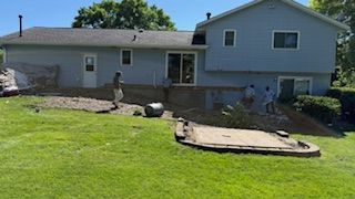 Backyard with a house, green lawn, stone path, and raised patio area on a sunny day