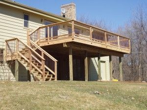 A large wooden deck with stairs leading up to it is in front of a house.