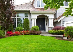 A light gray house with a well-manicured lawn and colorful landscaping.