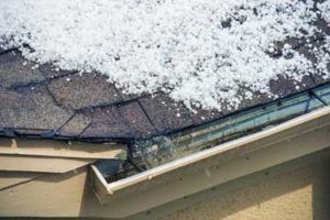 Hail covering a dark shingled roof and overflowing into the gutter.