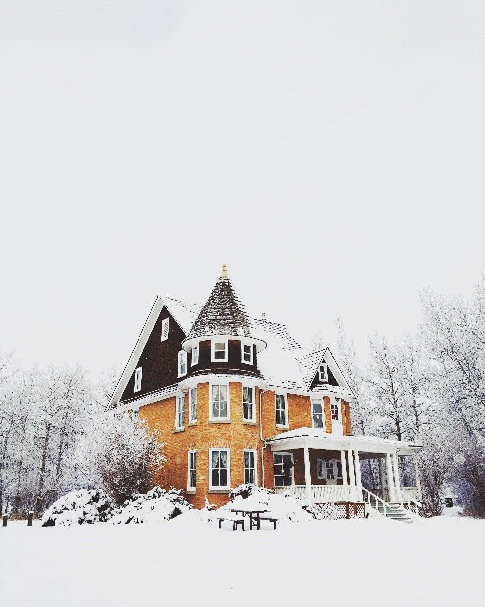 Yellow brick house with snow-covered roof and surroundings; trees and picnic table visible.