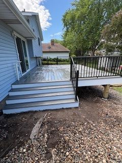 Outdoor wooden deck with steps, black railing, and a side view of a house with gravel below