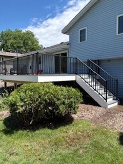 Raised backyard deck with black railing and stairs attached to a blue house on a sunny day