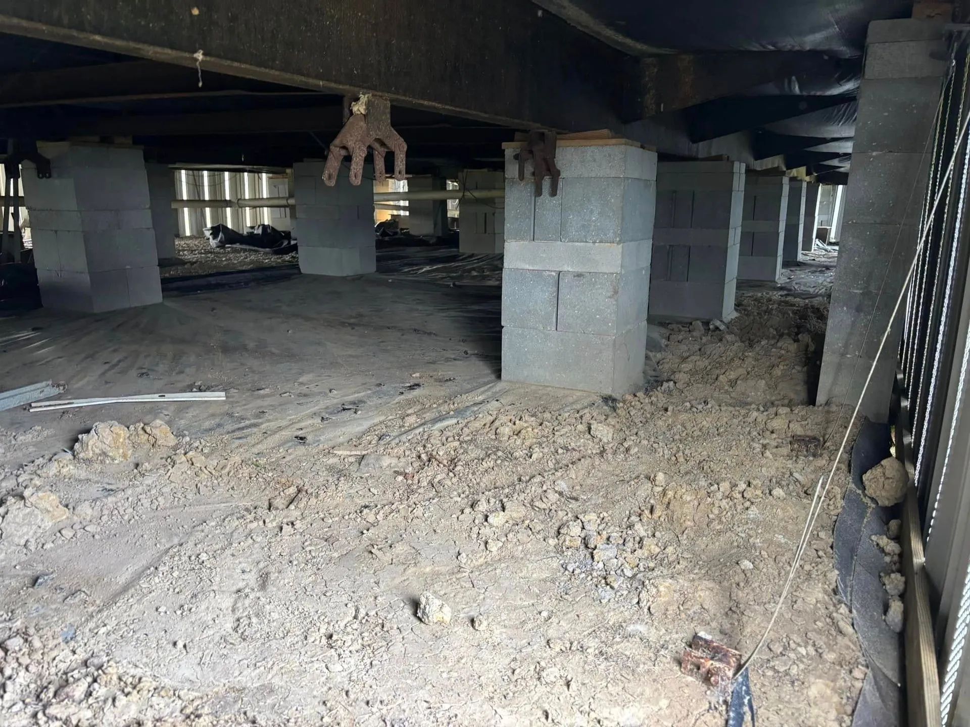 Underneath a mobile home: concrete block columns support a dark structure, dirt ground.
