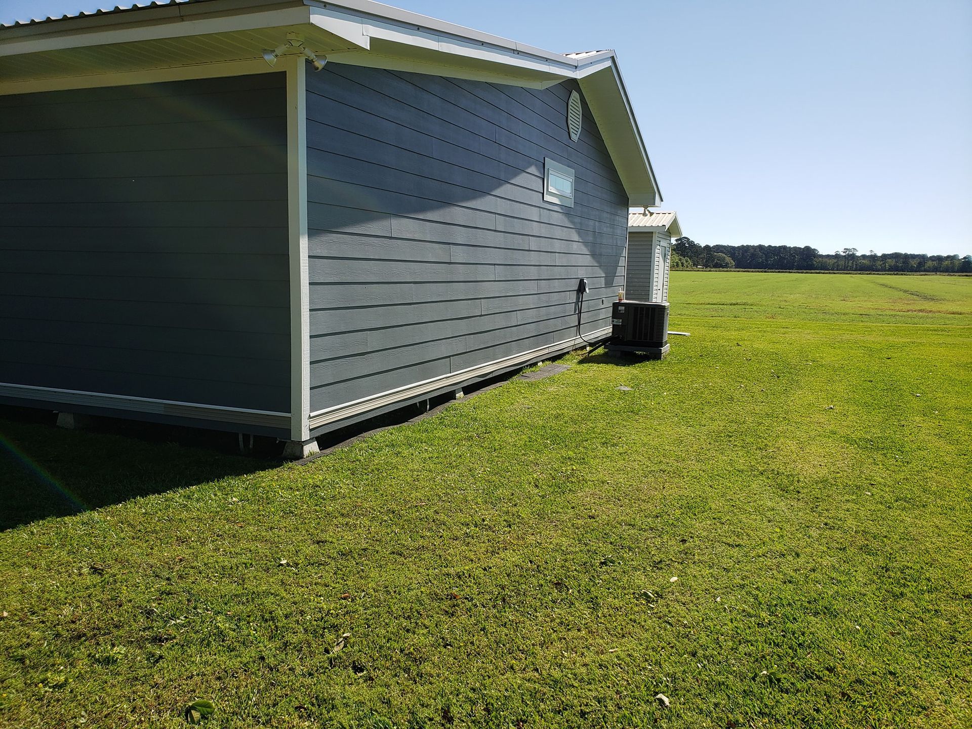 Grey house with white trim on a green lawn under a blue sky.