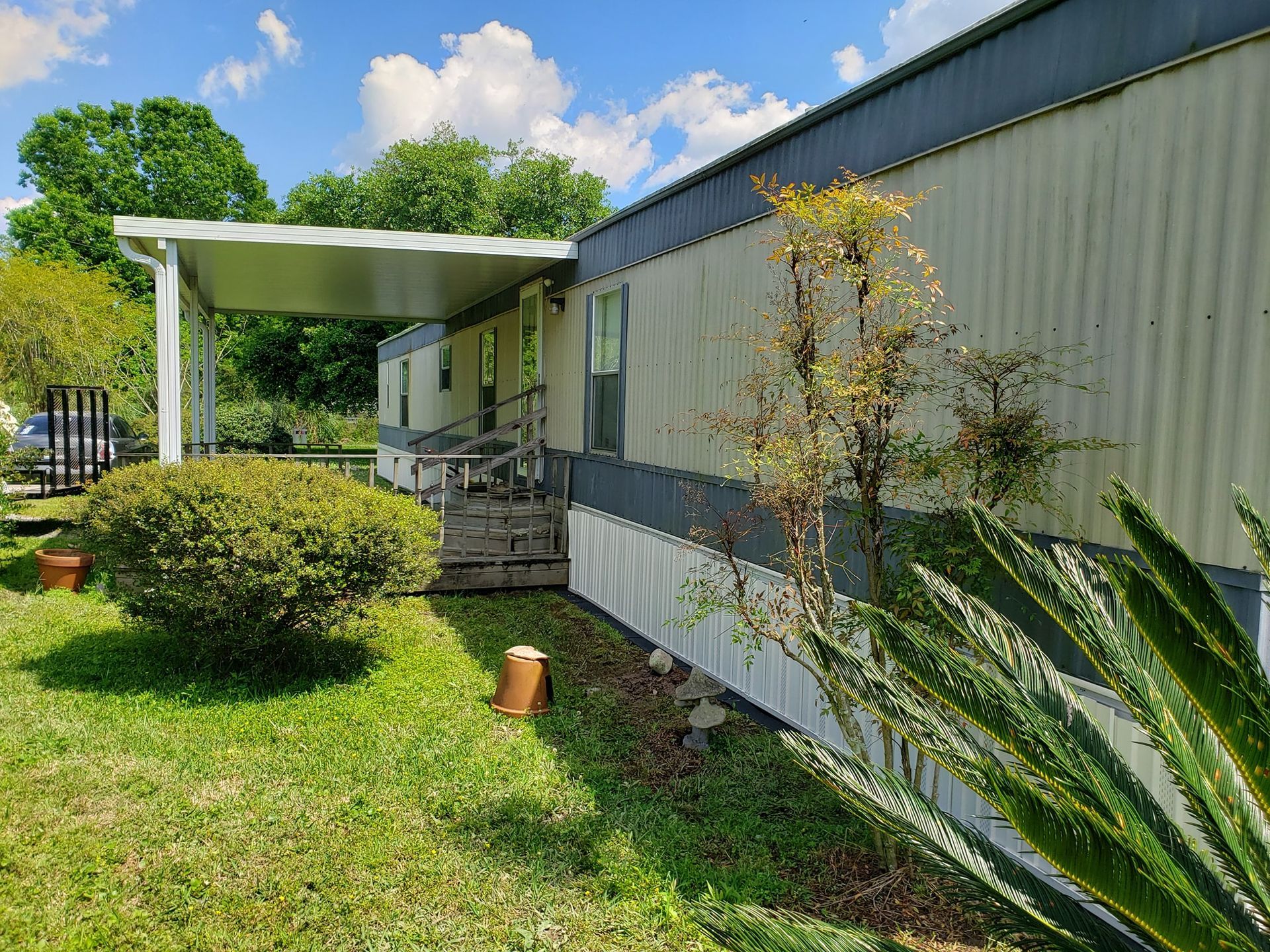 A mobile home with a porch and stairs is sitting in the middle of a lush green field.