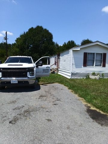 White pickup truck parked by a small white house with the driver door open on a gravel driveway.