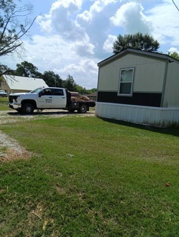 White pickup truck parked beside a mobile home on a grassy lot under a cloudy sky