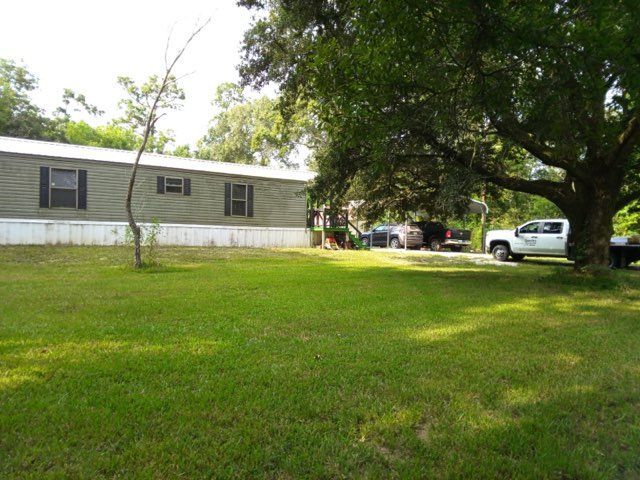 Grassy yard beside a mobile home with trees and a parked white pickup truck