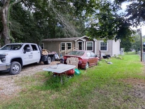 A man is kneeling down under a house while another man works on it.