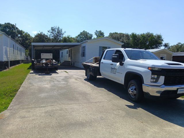 White pickup truck parked in a driveway beside a garage and trailer on a sunny day